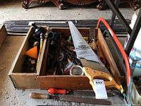 Box containing hand saw with yellow handle, various files, hammer, crowbar, oil can, screwdriver and assorted tools piled in wooden tray