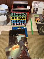 Front view of crate with stacked records and nearby plates; visible LPs arranged horizontally in front