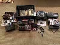 Complete view of the lot showing pens, push button phones, CDs, cash box, portable CD player, Curtis DVD player, DVDs, camera with case, and portable radio.