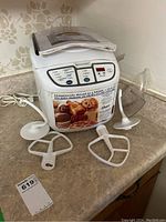 Full view of the Oster breadmaker with manual on top and three mixing paddles arranged around it.