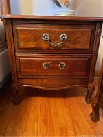 Front view of one night stand showing two drawers with ornate metal hardware and carved legs.