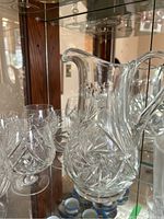 Photo showing clear large glass pitcher with handle and spout, surrounded by snifter glasses with cut pinwheel designs.