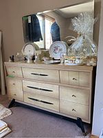Full view of the dresser with the large beveled mirror and various decorative items on top (not included). Shows nine drawers with different handle styles and black angled legs.