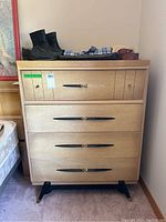 Full view of retro tallboy dresser showing 4 drawers with black blade handles, cream wood finish, and tapered legs with brass tips. Surface items not included.