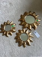 Three gold sunburst mirrors laid on carpet floor showing overall size and style