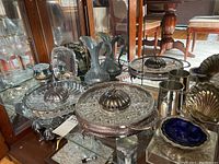 Display of silver-plated serving ware including footed bowl with flower frog, small serving tray, and pitcher.