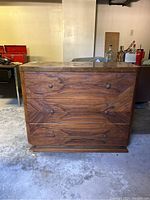 Front view of small three-drawer wooden dresser showing grain pattern, replaced knobs, and surface wear.