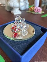 Clear crystal bear figurine holding red gift box on mirror base in blue box.