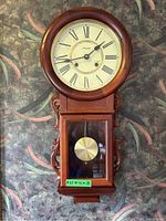 Front view of entire Spirit wall clock showing wood case, dial, lower door and pendulum bob.