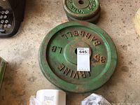 Photo showing 35 lb green cast iron weight plate with 'EVINE BARBELL YORK' markings, used condition with rust