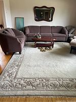 Living room setting showing the full cream and taupe bordered wool rug beneath sofa and coffee table.