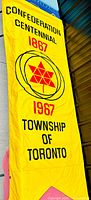 Full length shot of the yellow centennial banner showing text and central red maple leaf emblem.
