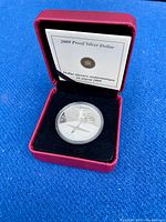 Red presentation case open showing the silver proof dollar coin in capsule with certificate behind it.