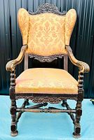 Front view of the antique armchair showing carved oak frame and upholstered seat and high backrest with padded winged sides.