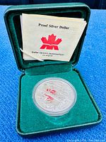 Silver proof dollar coin in green velvet case with certificate booklet visible behind the coin.