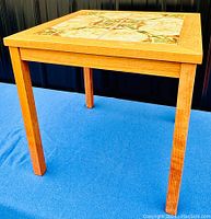 Full three-quarter view of square teak side table on blue backdrop
