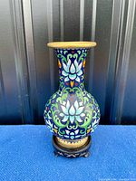 Front view of the vase showing colorful cloisonne lotus flower design, blue background, gilded rim and wooden base.
