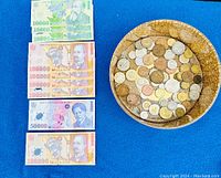 Romanian banknotes laid out on blue surface beside wooden bowl of mixed coins.