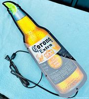 Front view of the Corona Extra beer bottle light-up sign with attached power cord and switch shown coiled.