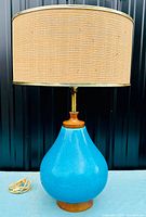 Full view of lamp with cerulean blue crackle glaze ceramic body, teak accents, brass stem, woven fabric drum shade, and cord