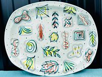 Front view of the oval serving platter showing full 'Primavera' pattern by Jessie Tait with stylized colorful botanical and geometric shapes on white speckled ceramic.