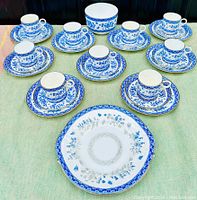 Full set of nine trios (cup, saucer, biscuit plate) arranged with the cookie platter and serving bowl. Blue and white floral bone china with detailed patterns.