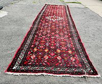 Full length view of the red geometric and floral patterned Persian runner rug laid on concrete showing overall design and condition.