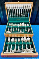 Photo shows the complete set of flatware items arranged inside a wooden case with green felt lining, highlighting various knives, forks, spoons, and serving pieces in the Modern Baroque pattern by Oneida Community.