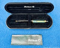 Pelikan green striped ballpoint pen in original black case with Pelikan Garantie booklet laid out on blue background.