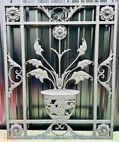 Full front view of black painted vintage cast-aluminum garden trellis featuring floral and leaf designs with a central urn motif.