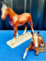Close-up of standing horse and lying foal porcelain figurines on blue fabric background