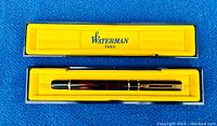 Wide view of the original black case lined with yellow fabric showing the Waterman Paris branding and the tortoise patterned fountain pen inside.