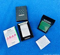 Two Zippo lighters displayed with original black packaging and product inserts on a blue surface.