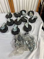 Lot showing eleven black rubber wheels on metal casters with threaded stems, some stacked, some loose, with small bags of hardware screws.