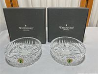 Two Waterford branded black boxes with two clear crystal bottle coasters in front, showing detailed cut glass star and floral patterns.