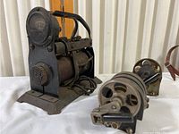 Angled view showing black metal rectifier with ammeter gauge and control knob alongside two smaller antique magnetos with gear mechanisms