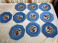 Full set of 11 blue fruit plates laid out on a surface showing overall condition and matching designs