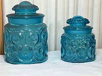 Photo of two blue glass canisters with lids, showing overall size and pattern details.