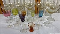 Large clear coupe-style glasses and smaller colored stemmed glasses arranged on a table.
