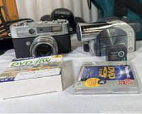 Photo showing the Yashica Lynx 500 camera and Panasonic VDR-M50 video camera with blank media discs and accessories.