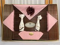 Lot includes cat-shaped ceramic salt and pepper shakers standing on brown bamboo placemats with pink napkins and one brown napkin ring.