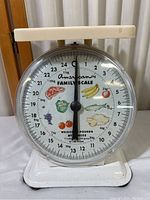 Front view of the vintage American Family Kitchen Scale showing large dial with colorful fruit, vegetable, and meat illustrations and weight graduations in pounds and kilograms.