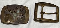 Two vintage brass or bronze belt buckles: one with a detailed elk head design and another plain rectangular frame buckle.
