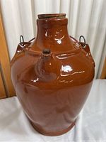 Front view of vintage brown glazed stoneware jug with cork stopper and small spout, metal handle attached near neck.