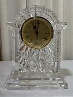 Front view of Waterford Crystal clock showing clear cut crystal body, base, and gold-tone clock face with roman numerals and three black hands.