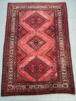 Full view of the Persian rug showing the triple medallion geometric design in abrashed shades of red and pink with patterned border.