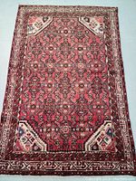 Full view of the Persian rug showing the all-over intricate pattern and four corner medallions, colors dominated by deep red and cream borders.