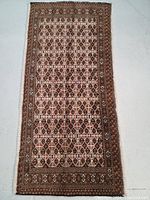 Full view of flat laid rectangular Turkmen wool rug with detailed geometric diamond pattern in beige, brown, red, and black, seen clearly on a concrete floor.