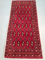 Top-down photo showing the entire rectangular hand knotted Persian Turkman wool rug with vibrant red background and geometric patterns.