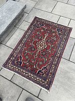 Full view of the small Hamadan rug placed outdoors on stone tiles, showing the rug's overall pattern and condition including minor wear
